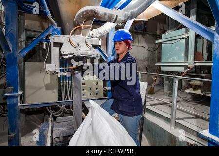 Taraz/Kasachstan - April 25 2012: Phosphordüngeanlage. Verpackungslinie. Eine junge Arbeiterin in blauem Schutzhelm auf Förderband. Stockfoto