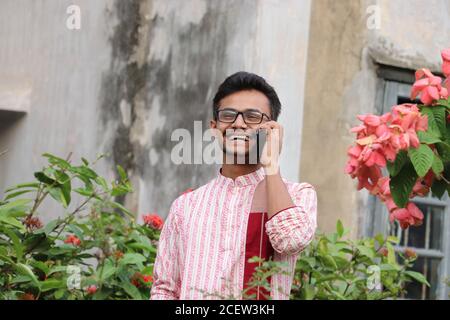 Lächelnder junger asiatischer Mann, der panjabi trägt und auf dem Handy spricht Draußen im Garten Stockfoto