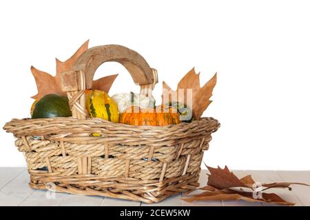 Kürbisse im Korb und Herbstblätter auf weißem Holztisch Stockfoto