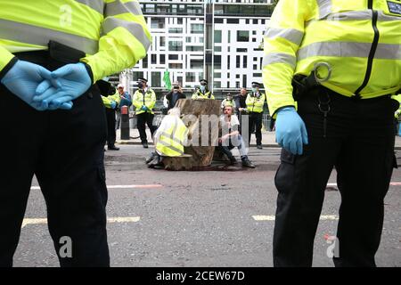 Polizeibeamte umgeben das Aussterben Rebellion Demonstranten, die miteinander durch ein großes Stück Holz vor dem Home Office in Marsham Street, Westminster, London geklebt werden. Stockfoto