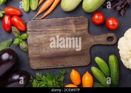 Sortierte rohe Bio-Gemüse und Schneidebrett auf dunklem Stein Hintergrund Erntezeit Vegetarisches Essen und Diät Konzept Draufsicht Speicherplatz kopieren Stockfoto