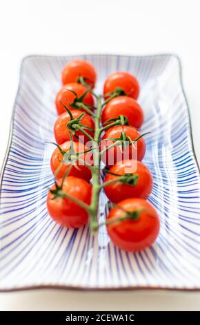 Eine horizontale Rebe aus Kirschtomaten auf einer Keramikplatte Stockfoto