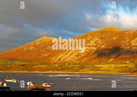 Wunderschöne Sonnenuntergangsbeleuchtung auf Bergen (Yr Eifl) mit Meer vor ihnen und dunklen Wolken in Trefor, Nordwales Stockfoto