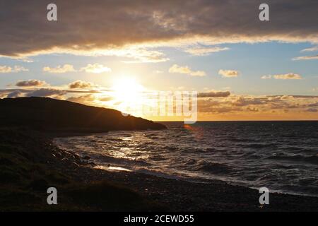 Schöner goldener, wolkig gedaber Sonnenuntergang über einer Meeresbucht und Landzunge in Trefor, Nordwales Stockfoto