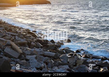 Wunderschöne, raue, schäumende Felsbrocken am Ufer bei Sonnenuntergang in Trefor, North Wales Stockfoto