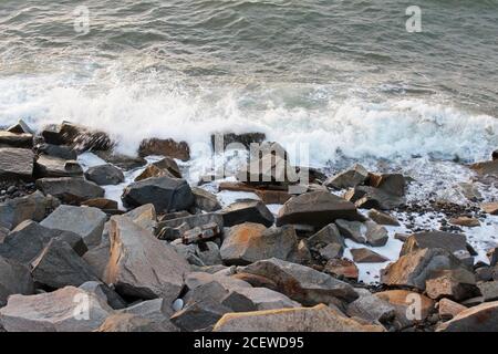 Wellen schlagen auf graubraunen Felsbrocken an der Küste von Trefor, Nordwales Stockfoto