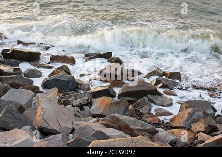Wellen schlagen auf graubraunen Felsbrocken an der Küste von Trefor, Nordwales Stockfoto