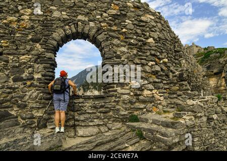 Wanderer mit Rucksack und Nordic Walking Stöcke bewundern die Aussicht von einer Öffnung in der Stadtmauer des Meeres Dorf, Porto Venere, La Spezia, Italien Stockfoto