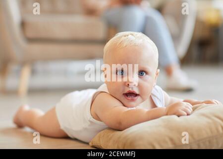 Horizontale mittlere Nahaufnahme des verspielten Babys, das Spaß hat Der Boden liegt auf dem Kissen, während seine Mutter auf dem Sofa sitzt Stockfoto