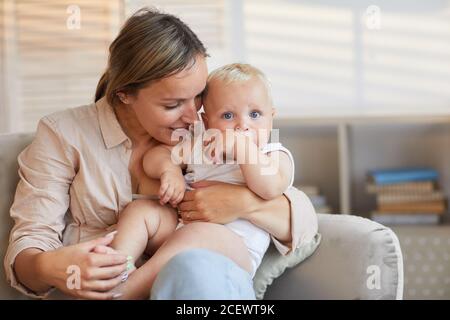 Horizontal Medium Porträt von attraktiven kaukasischen Frau tragen lässige Outfit sitzen mit ihrem Baby auf dem Schoß, kopieren Raum Stockfoto