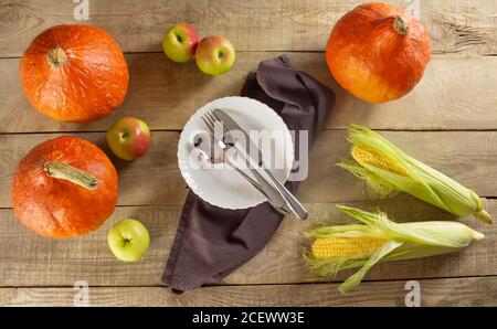 Happy Thanksgiving mit Kürbissen und Blättern, Obst und Gemüse auf dunklem Holzhintergrund. Teller und Besteck in der Mitte des Hintergrunds. Stockfoto