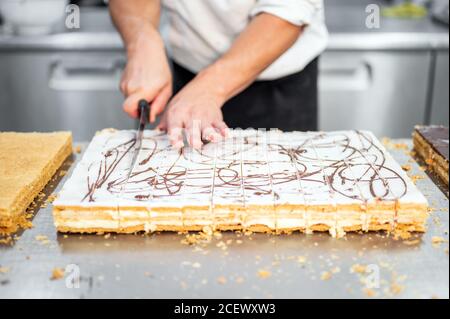 Nahaufnahme eines Konditors, der einen großen Kuchen in Portionen in der Konditorei schneidet. Hochwertige 4k-Aufnahmen Stockfoto