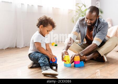 Junger afroamerikanischer Mann, der mit Bausteinen auf dem Boden spielt Mit einem kleinen Sohn Stockfoto