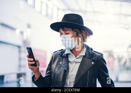 Junge trendige Frau in Maske mit Smartphone im Business-Center Während einer Pandemie Stockfoto