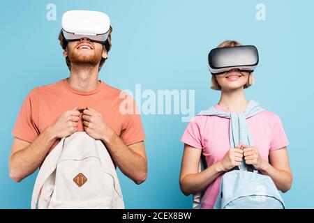 Junge Studenten in Virtual-Reality-Headsets halten Rucksäcke auf blau Stockfoto