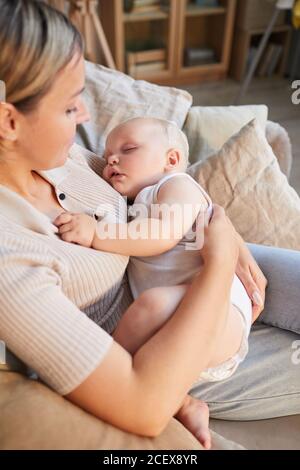 Vertikale High-Angle-Aufnahme der modernen kaukasischen Frau sitzt auf Sofa kuscheln ihr schönes Baby Sohn in den Armen Stockfoto