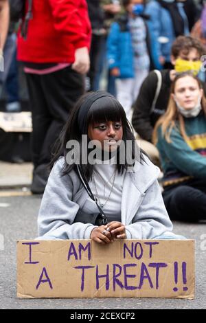 Ein junges Mädchen sitzt mit einem Plakat an der Million People March, London, 30 August 2020 Stockfoto