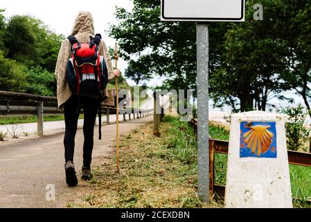 Rückansicht von einsamen unkenntlichen Wanderer mit Rucksack und Trekking Bleiben Sie auf dem Weg in der Nähe von Wegweiser mit Jakobsmuschel Symbol Von Camino de Santiago in Spanien Stockfoto