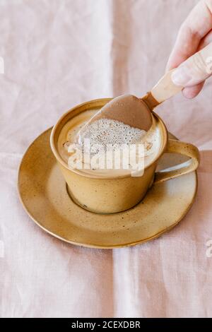 Von oben beschnitten unkenntlich Person Tauchen Eis auf Stick In Kaffee Tasse leckeren aromatischen Kaffee auf rosa Handtuch Stoffhintergrund Stockfoto