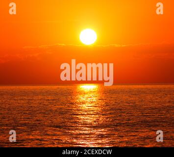 Sonnenuntergang mit orangefarbener Sonne und glitzerndem Wasser. Meereswasser Hintergrund. Stockfoto