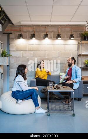 Gruppe von positiven jungen Menschen in lässiger Kleidung versammeln sich um Tisch mit Tassen Kaffee und diskutieren Pläne für neue Projekt während des Meetings im kreativen Coworking Space Stockfoto