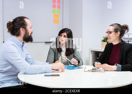 Ernst junge Mann und Frauen in formellen Kleidern sitzen an Tabelle und Notizen während der Zusammenarbeit an der Geschäftsstrategie Im modernen Coworking Office Stockfoto