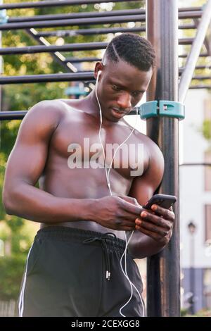 Muskulösen afroamerikanischen männlichen Athleten auf Sportplatz und stehen Auswählen von Melodien auf dem Smartphone für das Training Stockfoto
