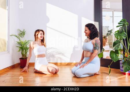 Fröhliche Freundinnen sitzen auf Holzboden in Vajrasana und Gemeinsam Yoga machen, während man sich anschaut Stockfoto