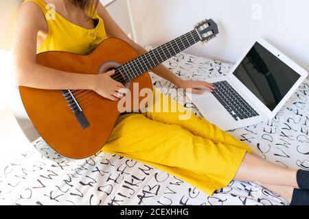 Cropped unkenntlich talentierte Frau sitzt auf dem Bett mit Gitarre und Online-Tutorial auf Laptop ansehen Stockfoto