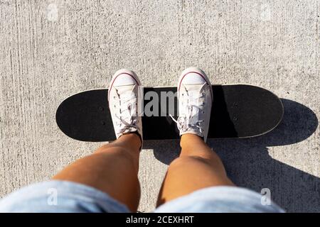 Von oben der Ernte anonyme Frau in Shorts und Sneakers stehen auf Skateboard auf Asphalt Straße während sonnigen Tag im Sommer Stockfoto