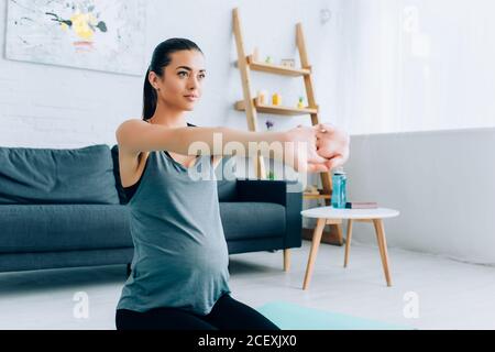 Schwangere Frau streckt die Arme auf der Fitnessmatte zu Hause Stockfoto