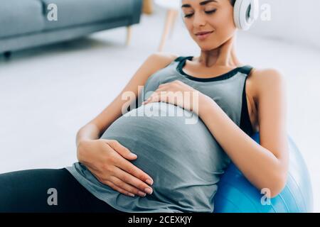 Gezielter Fokus der Sportlerin in Kopfhörern berühren Bauch auf Fitness Ball zu Hause Stockfoto