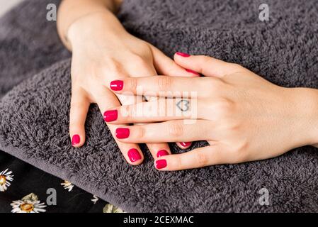 Von oben der Ernte unkenntlich weibliche Kundin mit hellem Rot Maniküre und Herz geformt Tattoo auf Finger entspannend während der Schönheit Sitzung im modernen Salon Stockfoto