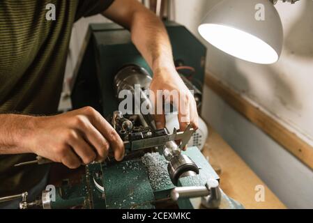 Nicht erkennbarer Techniker, der an der Werkbank steht und den Bremssattel für Präzision verwendet Messen während der Arbeit in einer schäbigen Werkstatt Stockfoto