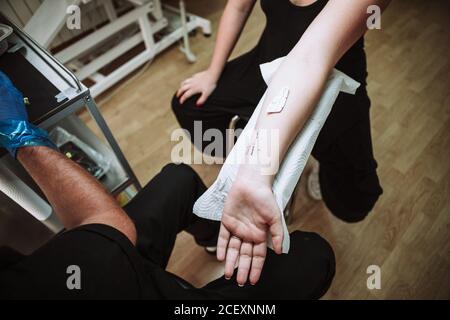Von oben der Ernte anonymen männlichen Tätowierer Vorbereitung für die Herstellung tattoo am Handgelenk der weiblichen Kunden in modernen Salon Stockfoto