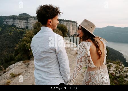 Rückansicht von glücklichen jungen Paar in stilvollen Hochzeitskleidung Lachend und einander anschauend, während sie zusammen gegenüberstehen Berglandschaft von Morro de Labella in Spanien Stockfoto
