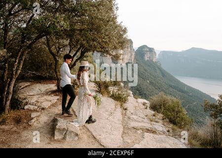 Seitenansicht von glücklichen jungen Paar in stilvollen Hochzeitskleidung Gemeinsam gegen die Berglandschaft von Morro de Labella in Spanien
