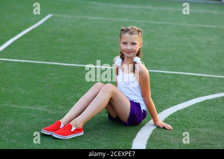 Das Mädchen sitzt auf dem Garn auf dem Sportplatz Stockfoto