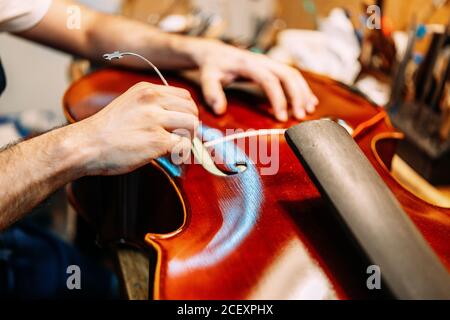 Crop anonyme Handwerker Einstellung Sound Post beim Bau Saiteninstrument In der Werkstatt Stockfoto