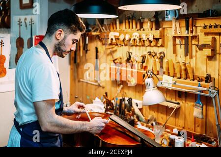 Seitenansicht des Handwerkers, der beim Bau einer Schnur einen Tonpfosten setzt Instrument in Werkstatt Stockfoto