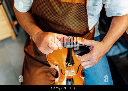 Hoher Winkel der Ernte anonyme Handwerker Geige mit Klemme halten Bei Restaurierungsarbeiten an der unteren Instrumentenabschwägung behoben Stockfoto