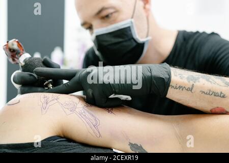 Crop männlichen Tätowierer mit Maschine macht Tattoo auf Arm der Frau auf dem Tisch im Salon liegen Stockfoto