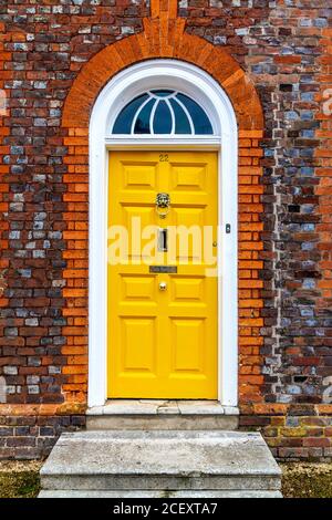 Eine leuchtend gelbe Tür mit Löwenklopfer in einem georgianischen roten Backsteinhaus, Baldock, Großbritannien Stockfoto