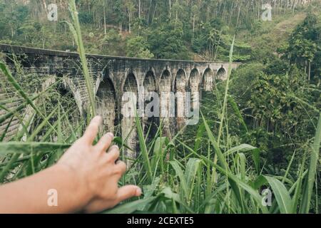 Crop anonymen männlichen Touristen erkunden Alter Stein Viadukt Nine Arch Brücke inmitten von grünen Hügeln während der Reise in Sri Lanka Stockfoto