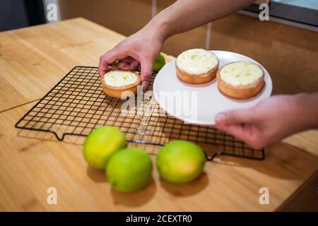 Gesichtslose Person, die köstliche Limettensorten mit Sahne auf Weiß arrangiert Platte über Holztisch Stockfoto