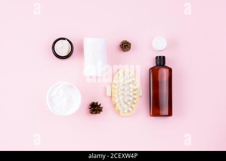Natürliches organisches Schönheitskonzept. Flasche mit Shampoo oder Kosmetiklotion, Handtuch, offenes Cremeglas, Massagegerät. Hautpflegeprodukte auf rosa Oberfläche. Kreativer Körper Stockfoto