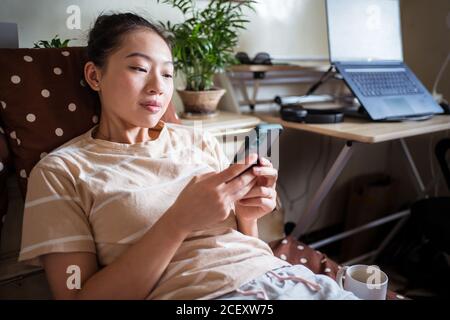 Frau, die im Schlafzimmer auf dem Bett sitzt und sich für das Essen entscheidet Mobile App über Smartphone beim Online-Shopping Stockfoto