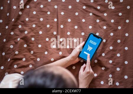 Von oben der Ernte anonyme Weibchen liegend auf dem Bett und Verwendung der Online-App auf dem Handy für die Bestellung von Lebensmitteln Stockfoto