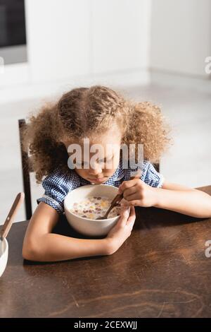 High-Winkel-Ansicht der afroamerikanischen Mädchen hält Löffel in der Nähe Schüssel mit Milch und Cornflakes Stockfoto