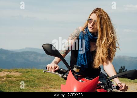 Brutal weibliche Biker sitzt auf dem Motorrad auf sandigen Straße in Sommer und wegschauen Stockfoto